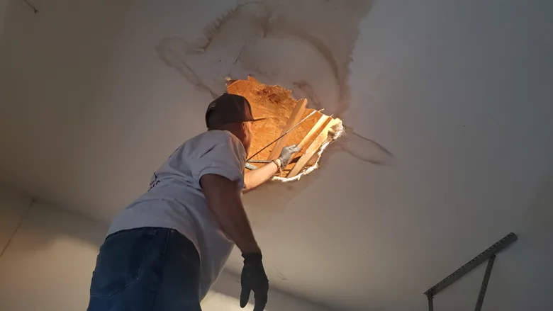 Technician inspecting an opening in a damaged ceiling