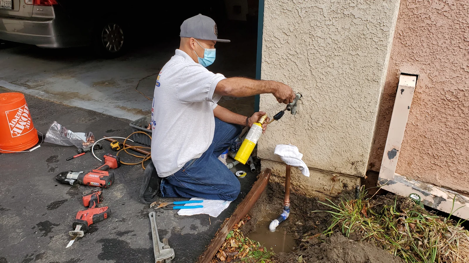 Plumber working on an exterior water pipe beside a home