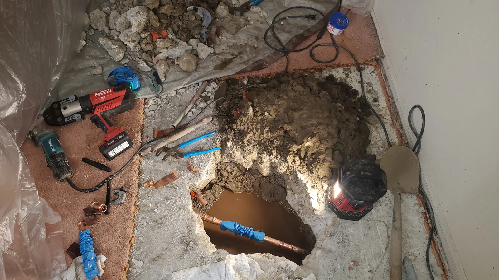 Exposed pipe and repair tools at an opening in a concrete floor